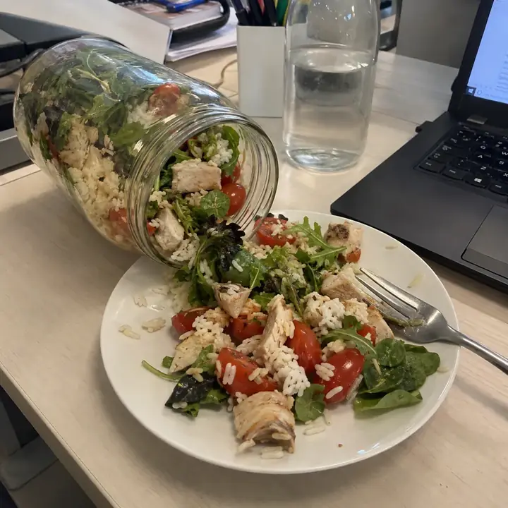 Ensalada de un tarro volcada en un plato sobre la mesa de la oficina, junto al teclado